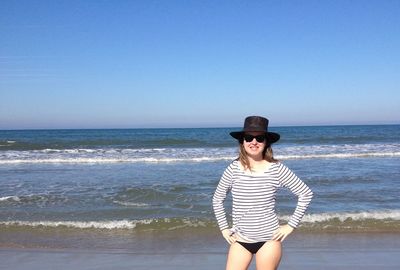 Smiling woman wearing hat and sunglasses while standing on shore against sky