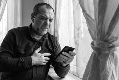Unhappy man with a smartphone in a room by the window. bad news concept