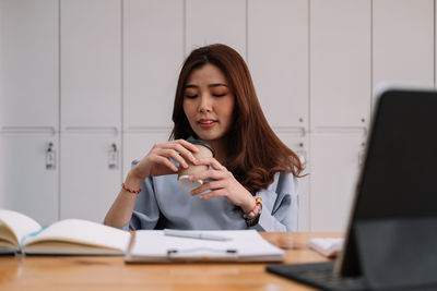 Young woman using phone while sitting on table