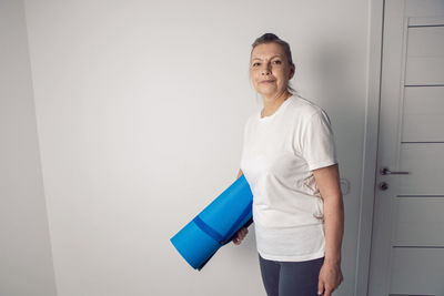 Woman aged athlete stands in a white room with a yoga mat