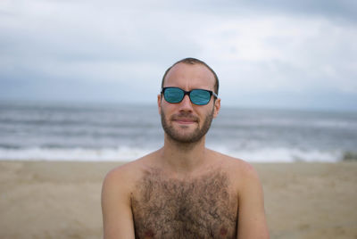 Man wearing sunglasses standing at beach against sky