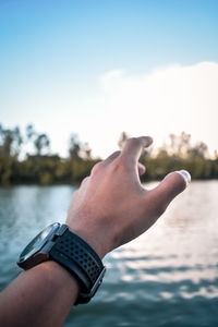 Cropped hand reaching lake against sky