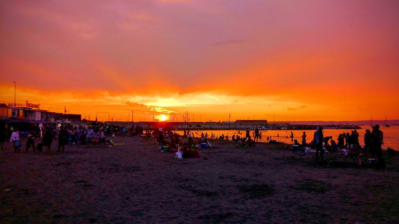 GROUP OF PEOPLE ON BEACH AGAINST SKY DURING SUNSET