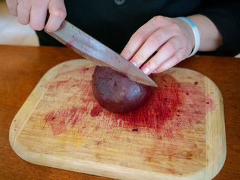 Cropped hands of person cutting common beet in kitchen
