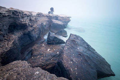 Man standing on cliff by sea against sky