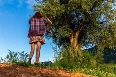 Low angle view of woman standing by tree against sky