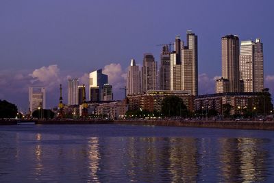 Modern buildings by river against sky in city