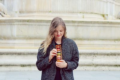 Young woman with macaroons standing against wall