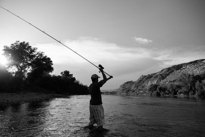 Man fishing in river against sky
