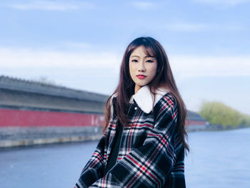 Portrait of beautiful young woman standing against sky