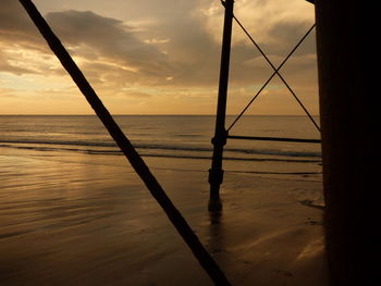 Scenic view of pier at beach against cloudy sky during sunset