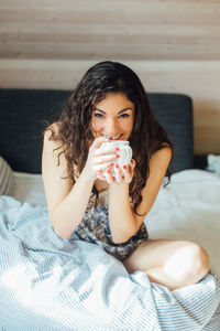 High angle portrait of young woman having coffee while sitting on bed at home