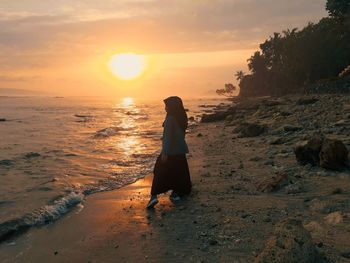 Woman standing on beach against sky during sunset