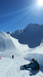 Snowboarder sitting on snow against sky