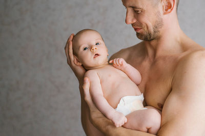 A young father holds his newborn son in a diaper in his arms