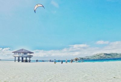 Kiteboarding over lifeguard hut at beach against sky during sunny day