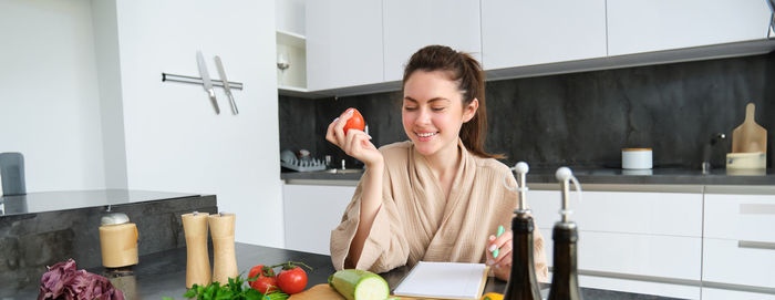 Portrait of young woman using mobile phone in kitchen