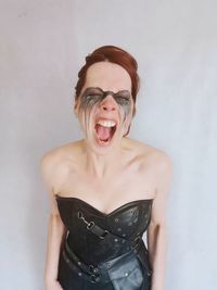 Young woman with face paint shouting while standing against white background