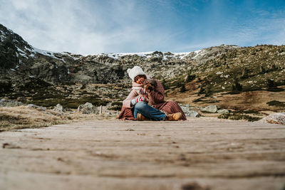 Couple sitting on mountain against sky