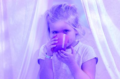 Portrait of girl having drink in cup against curtain