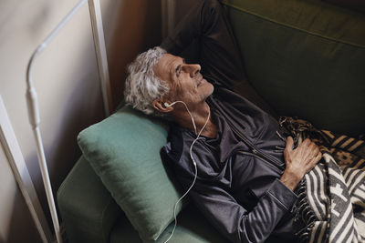 Senior man relaxing while listening music through in-ear headphones on sofa at home