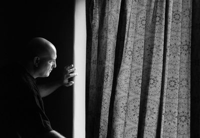 Side view of mature man looking through window at home