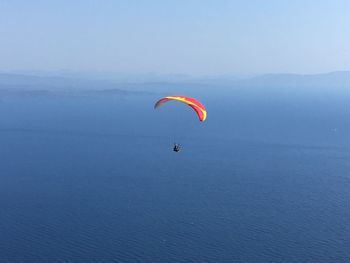 Person paragliding over sea against sky