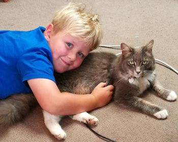 Portrait of cute boy with cat lying on carpet