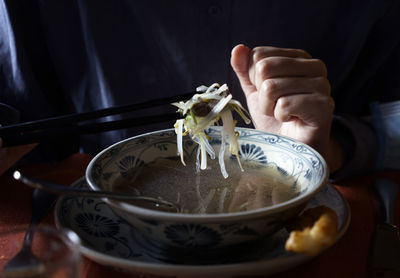 Person picking vegetables from a pho soup broth by chopsticks