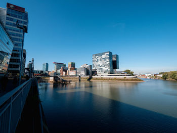 Buildings by river against clear blue sky