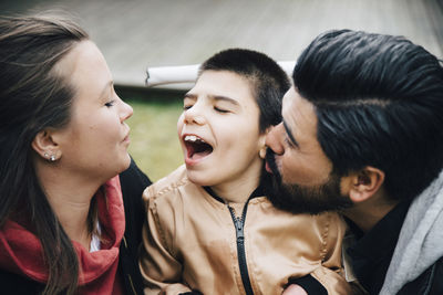 Father kissing happy son looking at his mother in yard