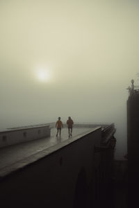 Rear view of people walking at beach against clear sky during sunset