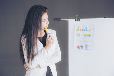 Young woman looking away while standing against wall