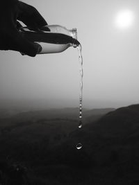 Close-up of person hand on water against sky