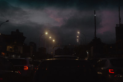 Cars on illuminated city street against sky at night