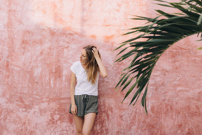 Young woman standing against wall bending the head and touching her hair 