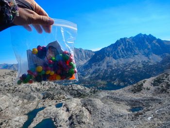Cropped hand of woman holding multi colored candies against mountain an sky