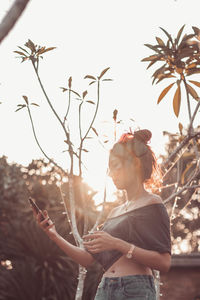 Low angle view of woman using mobile phone while standing against clear sky during sunset