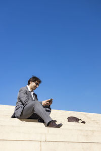 Man sitting on smart phone against clear blue sky