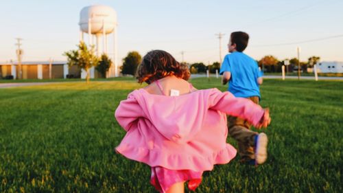 Rear view of girl with brother running on grassy field