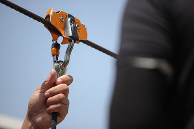 Low angle view of hand holding zip line pulley against sky