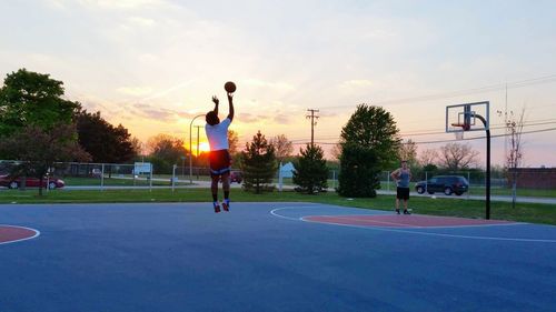 Men playing basketball on field against sky during sunset