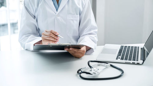 Midsection of doctor writing in clipboard at hospital