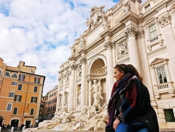 Side view of young woman looking away while sitting against old building