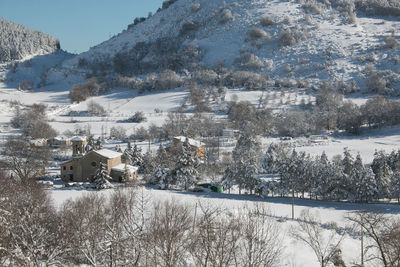 Snow covered houses by trees and mountains