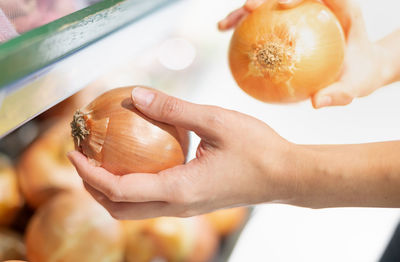 Female hand holding onion choosing for prepare the material food in the basket shelf in supermarket.