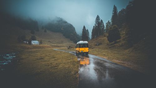 Wet road amidst trees against sky during rainy season