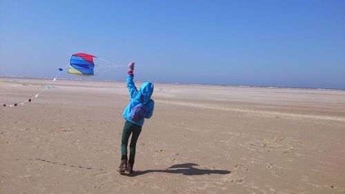Rear view of girl flying kite at beach against clear sky
