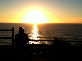 Silhouette man looking at sea during sunset