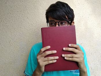 Portrait of woman reading book against wall